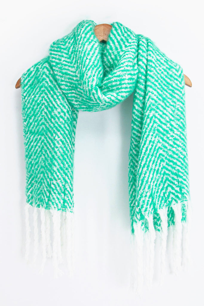 showing the green and white herringbone pattern winter scarf draped around a coat hanger, showing how it would look when worn.