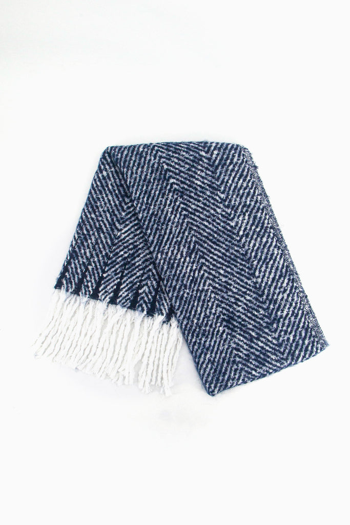 showing the scarf folded while laying flat, the navy blue herringbone pattern is clear as is the white tassel trim.