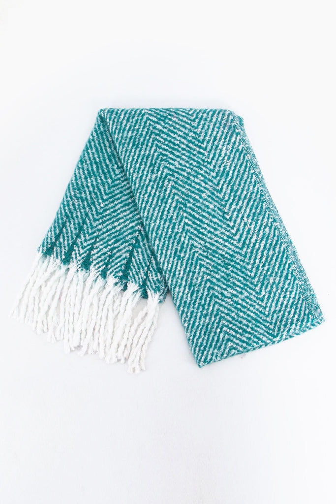 showing the scarf folded while laying flat, the turquoise herringbone pattern is clear as is the white tassel trim.