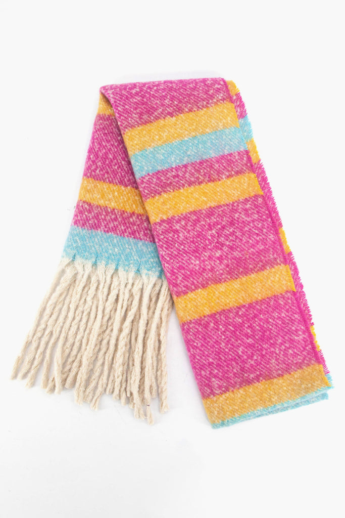 showing the scarf folded while laying flat, the fuchsia pink, yellow and blue striped pattern is highlighted as is the cream tassel fringe