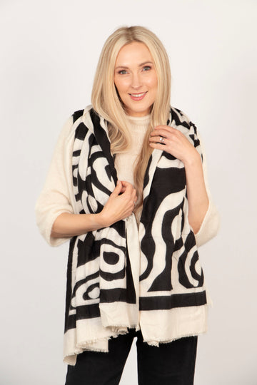 model wearing a black and cream abstract pattern scarf, accessories with a cream knit jumper and black trousers