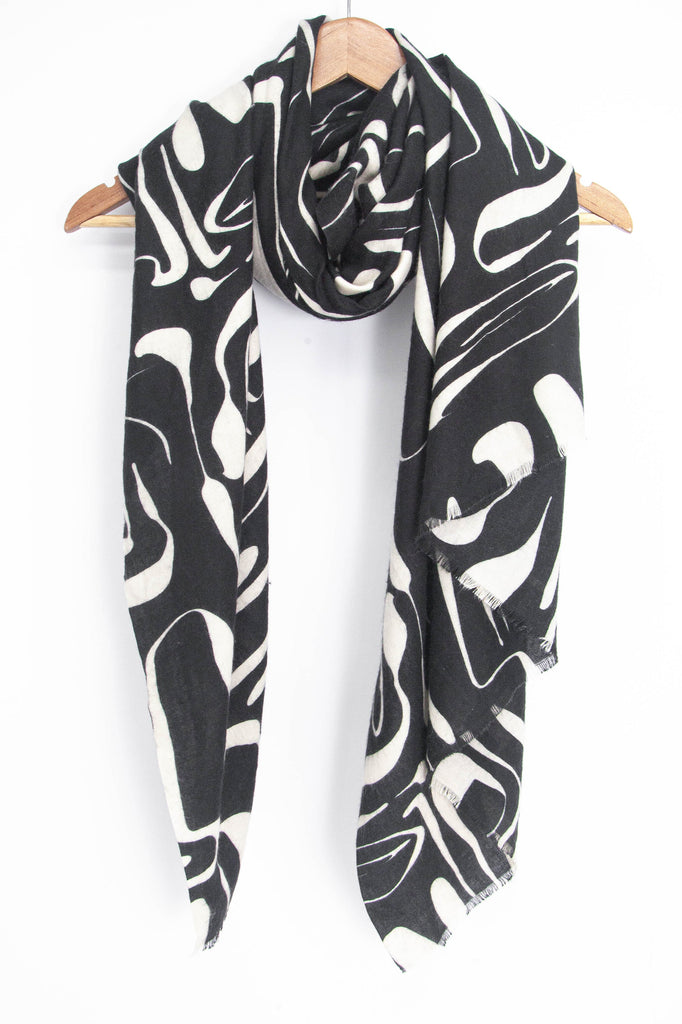 showing the black and white abstract pattern lightweight scarf draped around a coat hanger, showing how it would look when worn.