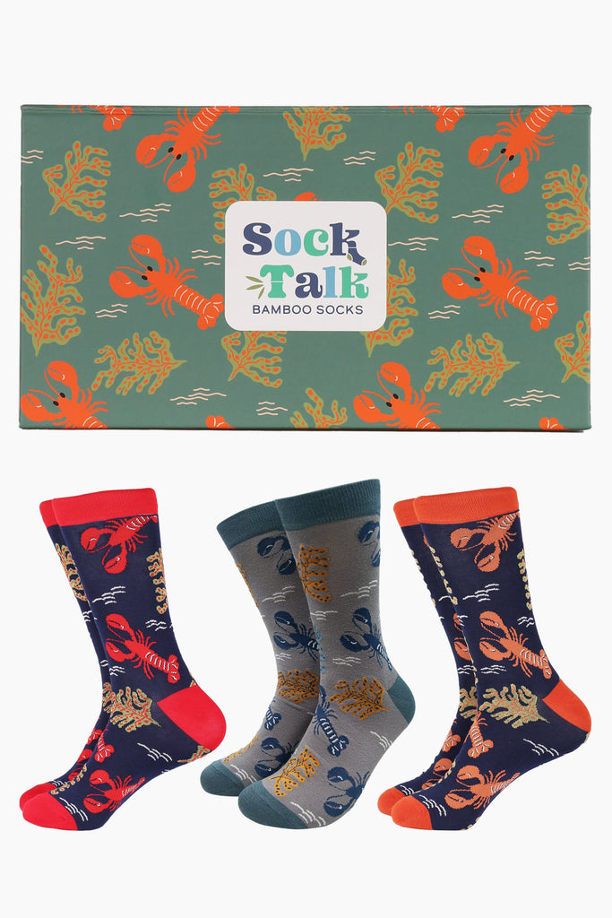 three pairs of lobster themed bamboo socks in a matching lobster themed gift box. the socks are blue and grey and feature an assortment of red, blue and orange lobsters in with coral and marine plantlife. the box is green with red lobsters all over