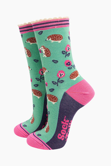 mint green bamboo socks with an all over pattern of woodland hedgehogs and pink pansy flowers. the socks have a contrasting pink heel and toe, the sole is navy blue. the cuff is scalloped and is pink and navy striped.