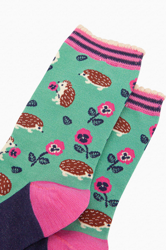 close up of the pattern. the hedgehogs are brown and beige, some are sitting holding pink pansy flowers, others are walking among the flowers. 