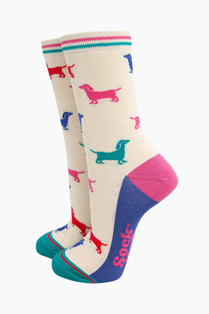 cream bamboo socks with a pattern of colourful sausage dogs. the sole is blue, heel is pink and the toe is turquoise. the cuff of the socks is straight cut and has a turquoise and pink stripe.