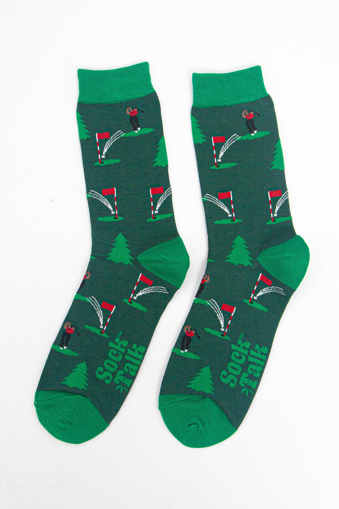 showing the socks laying flat, the golfer chipping the ball into the hole is visible all over the socks, there are also evergreen trees in the pattern