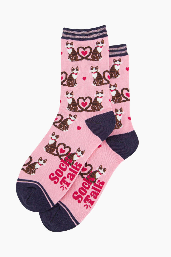 the pair of pink cat and love heart socks laying flat, one overlapping the other. showing clearly the light pink background of the socks which is contrasted by the all over pattern of cats and hearts. the sock talk logo is visible on the base of the sole. 