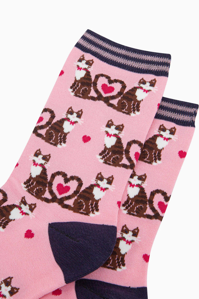 close up of the pattern. the cats are brown tabby striped and are wearing pink bow ties. Their tails are entwined in a love heart shaped loop. in the centre of the loop is a fuchsia pink love heart. there are smaller fuchsia pink love hearts scattered among the cats.