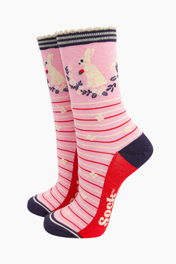 pink rabbit, wreath and strawberry bamboo socks. light pink bamboo socks with red and cream. on the ankle of the socks there is a white rabbit holding a strawberry. the wreath around the rabbit is navy blue and white.