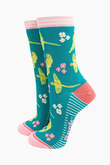 teal bamboo socks with a pattern of flying and perching ring necked parakeets and flowers. the heel and toe are a light coral pink, the cuff is pink and white striped.