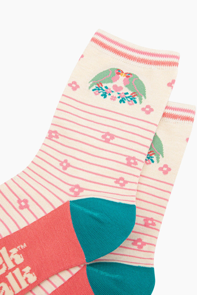 close up of the pattern. there are two green and pink love birds kissing with their beaks. they are perched on a branch of blue leaves and pink flowers. in between the love birds there is a pink love heart. 