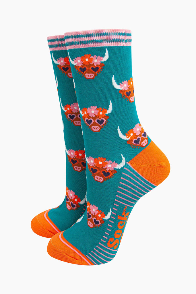 teal bamboo socks with an all over pattern of highland cows wearing floral crowns and love heart shaped sunglasses.