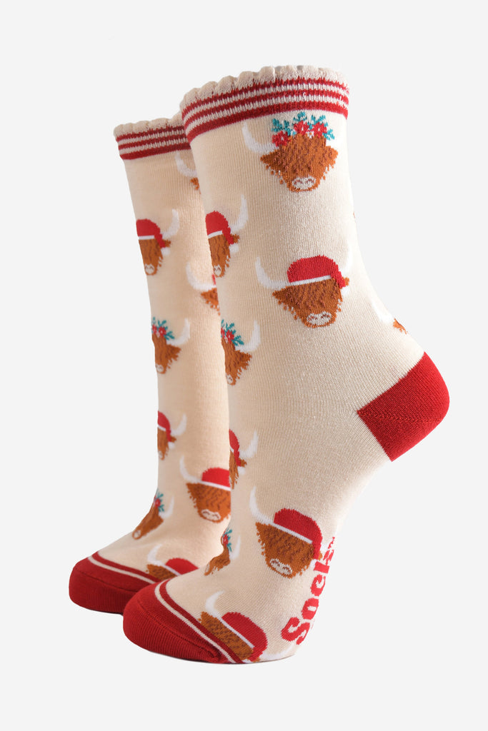 cream socks with red heel, toe and striped cuff featuring a pattern of highland cows wearing santa hats and floral crowns