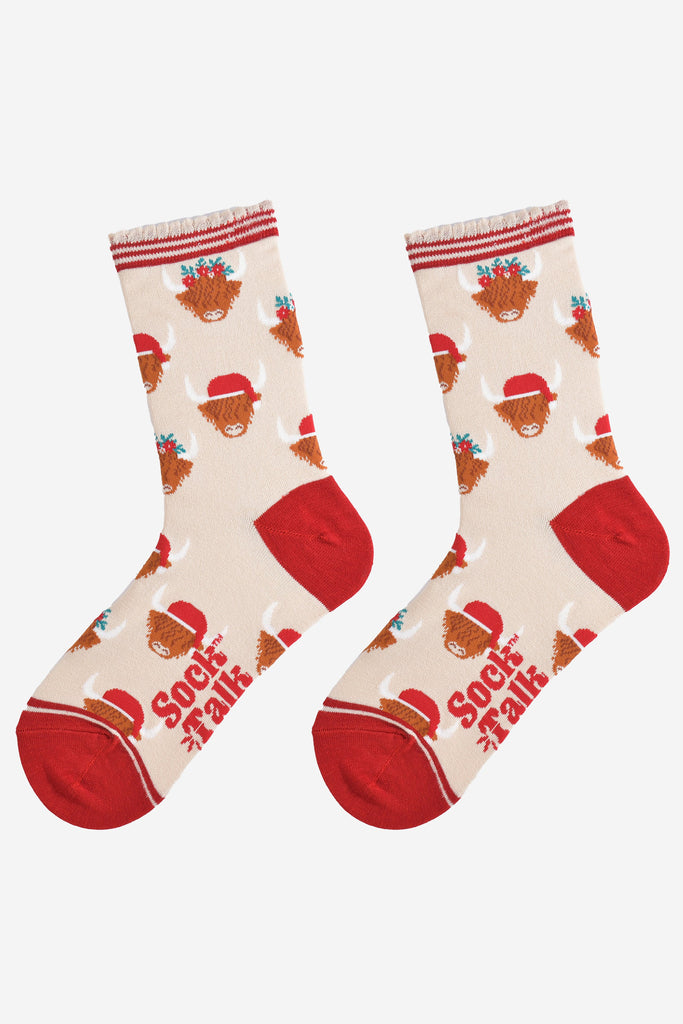 cream and red highland cow bamboo socks laying flat, showing the all over pattern of highland cows wearing santa hats and festive garlands