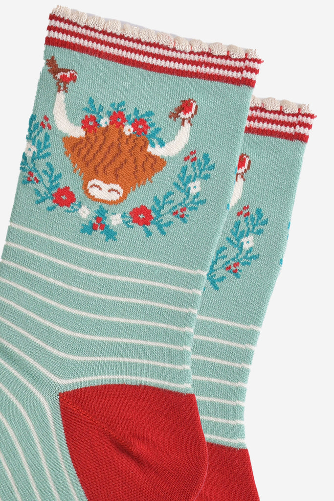 close up of the highland cow design on the ankle of the socks, there are robins perched on the tips of the horns, the wreath is green, red and yellow floral design
