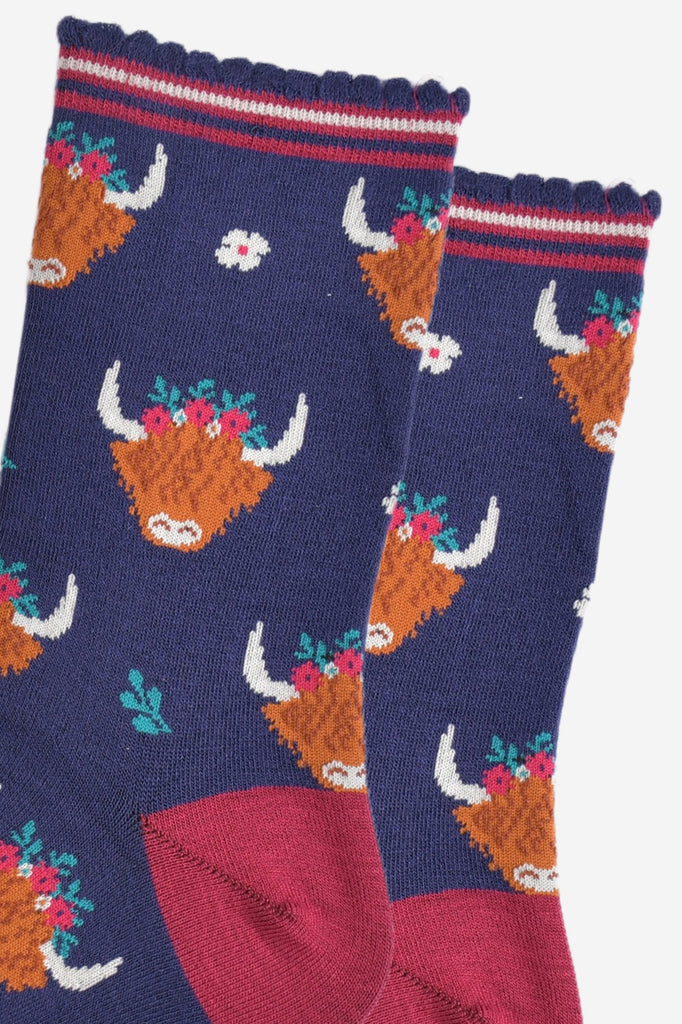 close up of the highland cow pattern on the socks, the cows are wearing green, red and white floral crowns, there are also small white flowers and green leaves on the socks