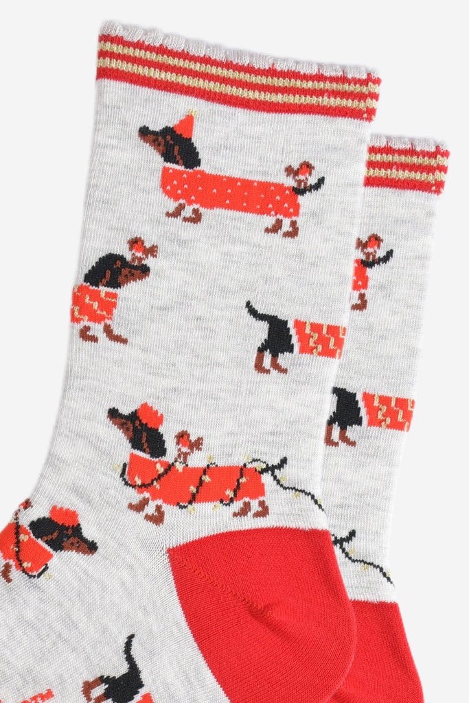 close up of the sausage dog pattern, the dogs are black and wearing red coats. one dog is wearing a red party hat and has a robin on its back. one dog is wrapped in gold party lights and is wearing a red party crown, also with a robin on its back. the last design is a dog wearing a red and gold coat and has a robin sitting on its nose.