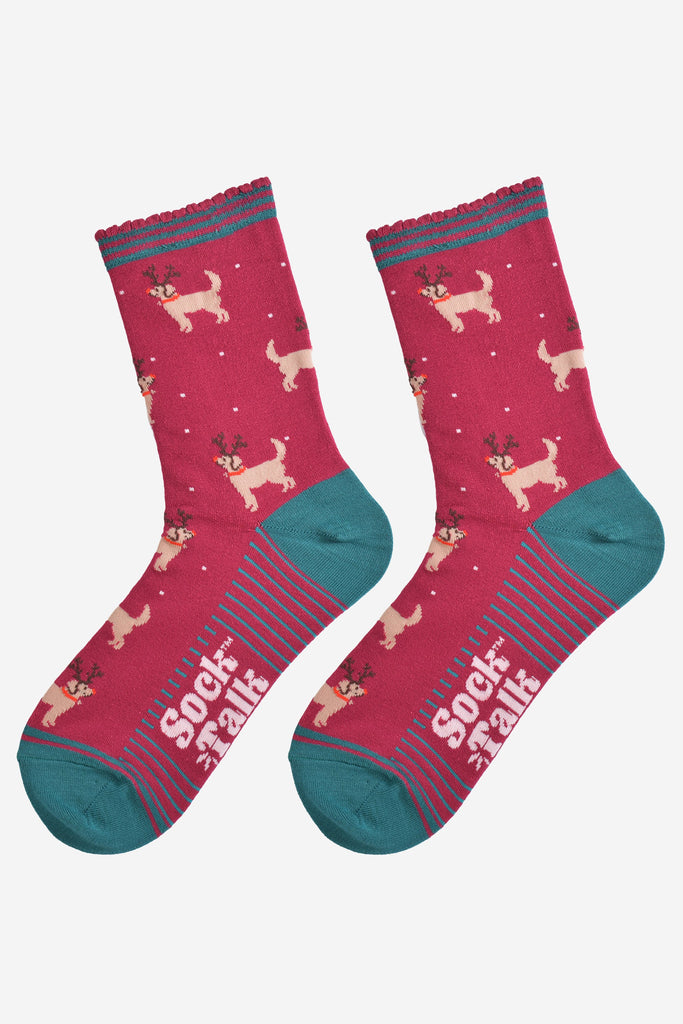 showing the golden retriever socks laying flat, the soles have green stripes, the dog pattern is all over the socks and there are also subtle falling snowflakes.