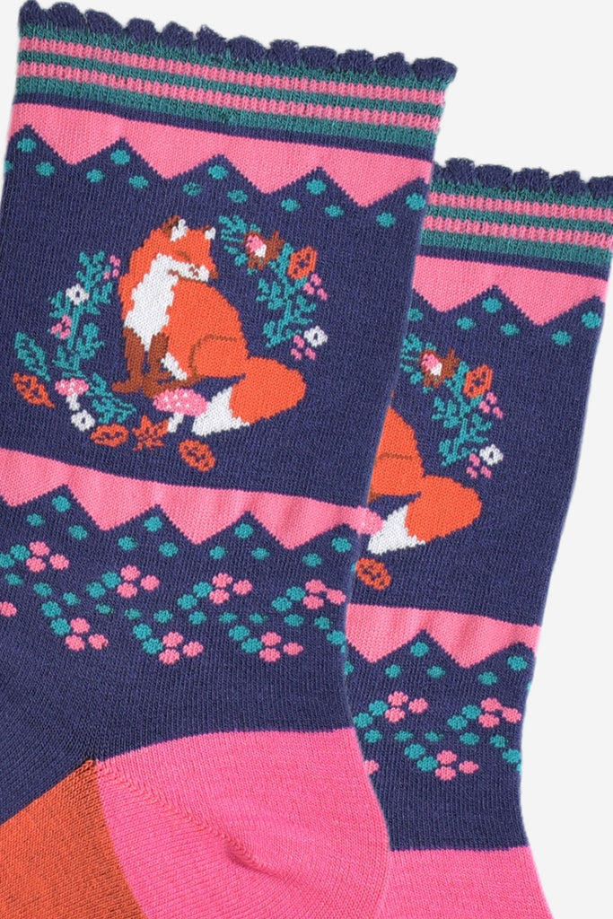 close up of the red fox and autumn foliage design on the ankle of the socks, there are also pink toadstools in the design, the fox is sitting and its tail is prominent