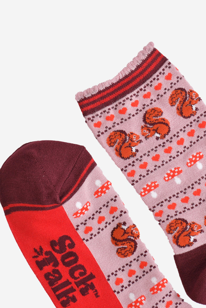 close up of the toe and cuff of the socks, the toe is burgundy with a red striped outline, the cuff is scalloped with a light pink edge and red and burgundy striped trim