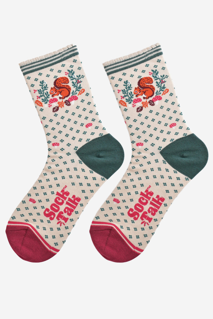 cream and green squirrel wreath socks laying flat, showing the all over green floral pattern and dominant red squirrel and wreath design on the ankle of the socks