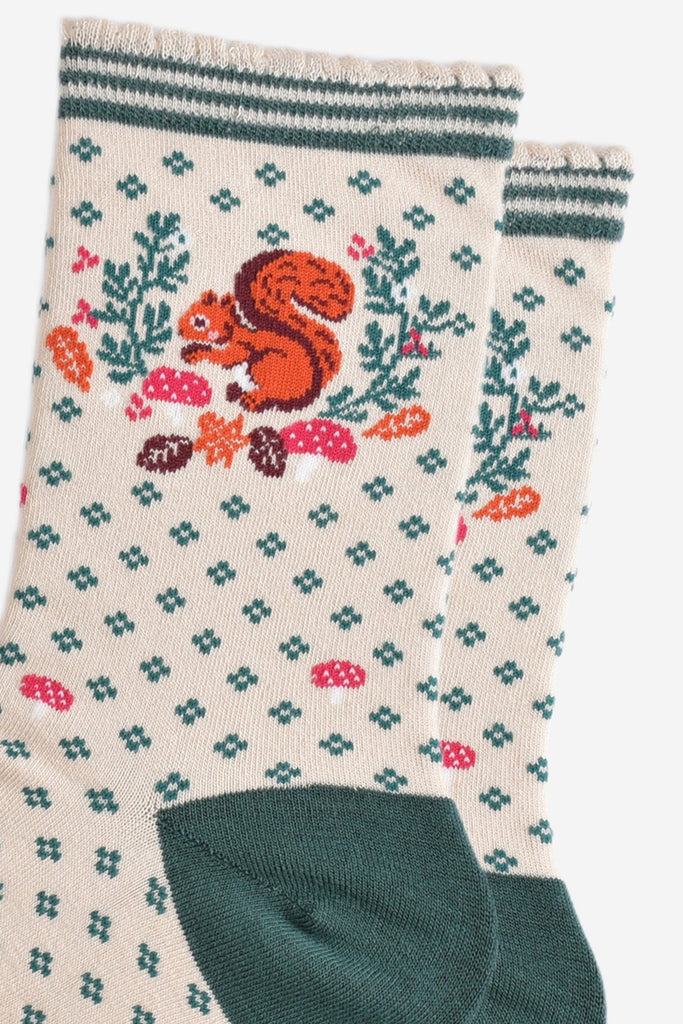 close up of the red squirrel and autumn foliage design on the ankle of the socks, the squirrel is holding an acorn and posed like it is foraging, it is surrounded by autumn leaves and pink toadstools