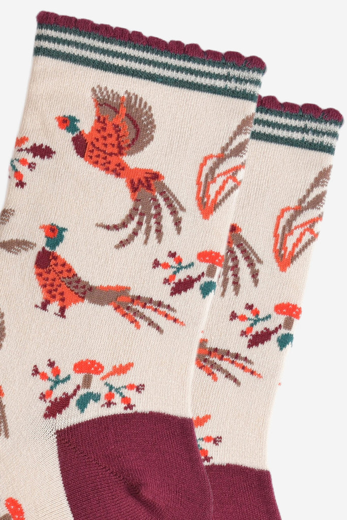 close up of the pheasants, they are illustrated in orange and red and appear to be walking and flying, surrounding the pheasants are autumn leaves and red toadstools