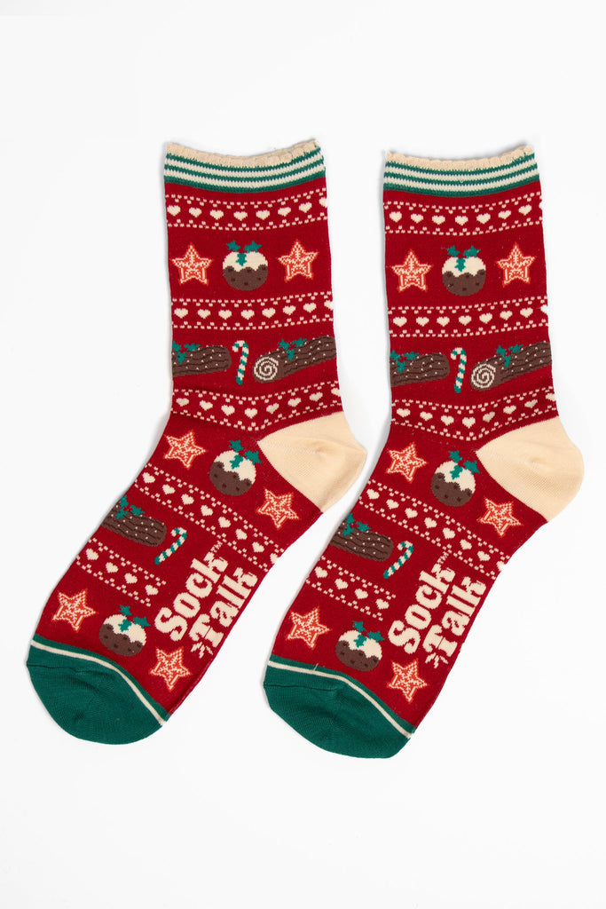 showing the christmas pudding fair isle socks laying flat. the christmas treats are in rows, separated by white dots and love hearts. The socks have a cream heel and green toe in contrast to the red background of the socks.