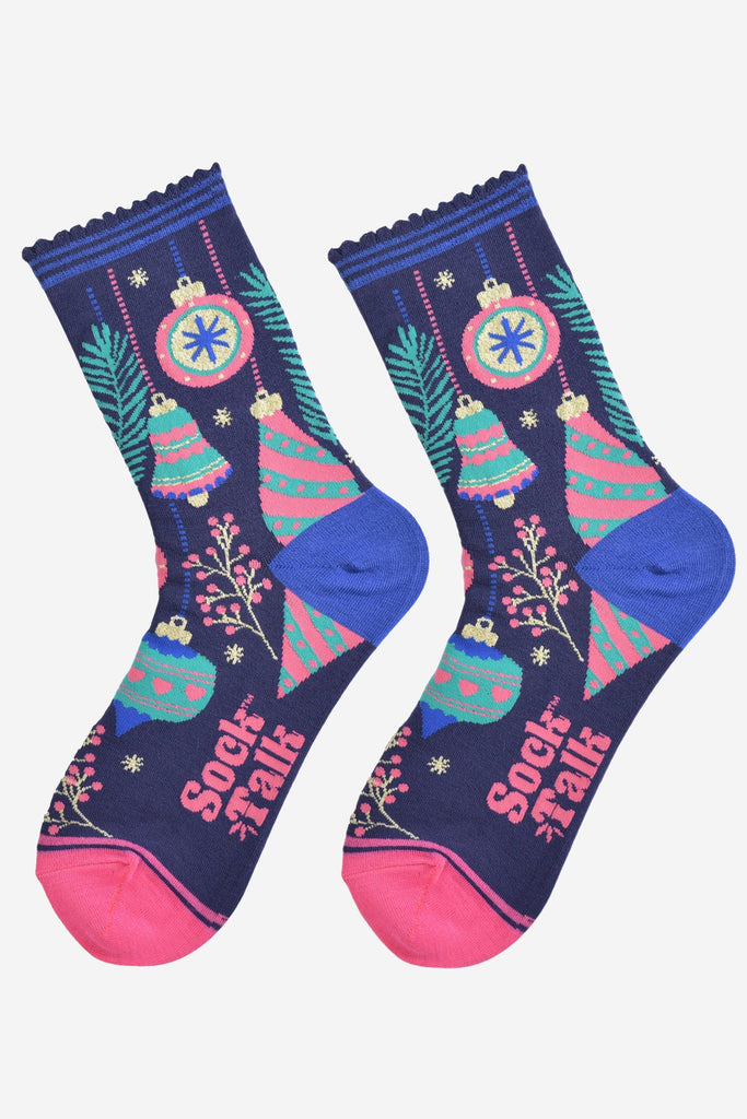 christmas tree bauble socks laying flat, showing an all over colourful design in blue, green and pink. there are festive baubles, xmas tree bells, small tree branches and berries.