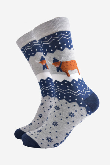 navy blue and grey bamboo socks with a fair isle zig zag and snowflake pattern, featuring a highland cow standing in a snowy field wearing a blue winter hat