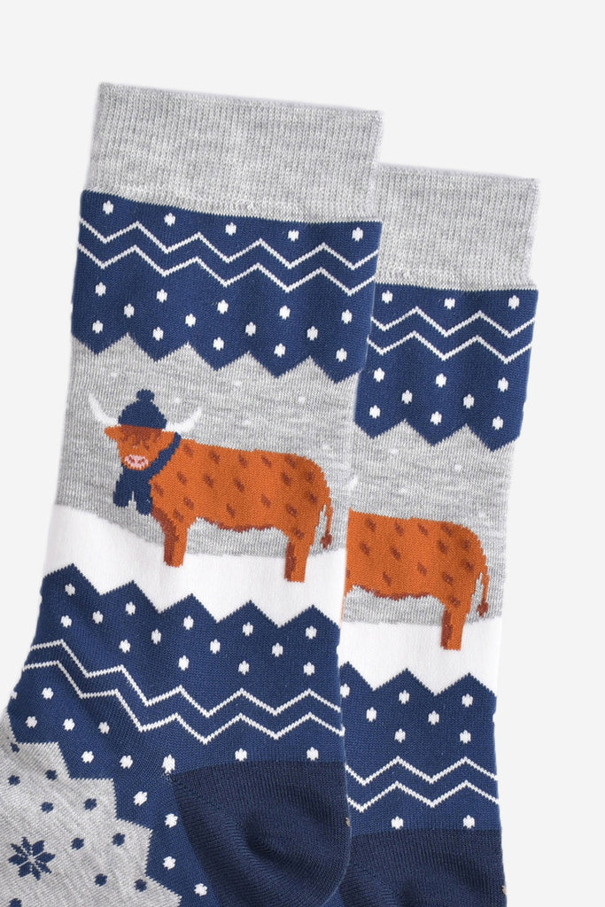 close up of the highland cow, it is standing in the snow and wearing a winter hat and scarf