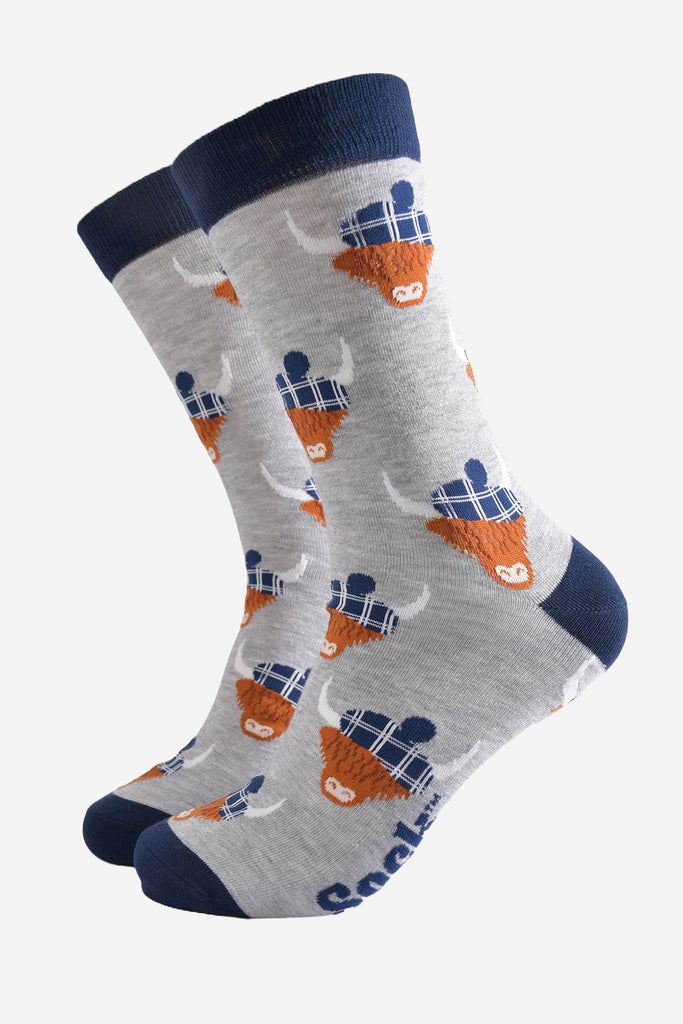 light grey socks with a navy blue heel, toe and cuff with an all over pattern of highland cows wearing tartan pom pom hats