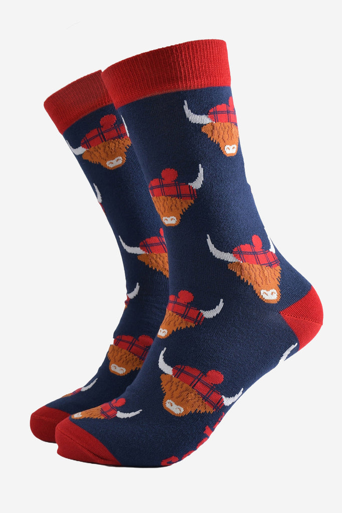 navy blue socks with red heel, toe and cuff with an all over pattern of highland cows wearing tartan pom pom hats