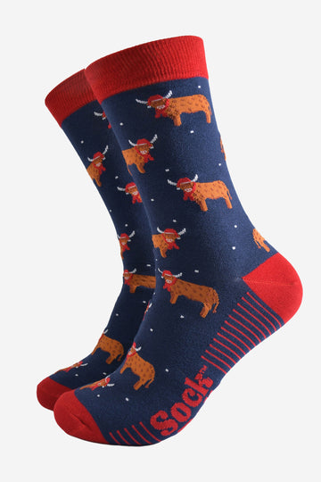 navy blue socks with a red heel, toe and trim with an all over pattern of highland cows wearing santa hats and winter scarves