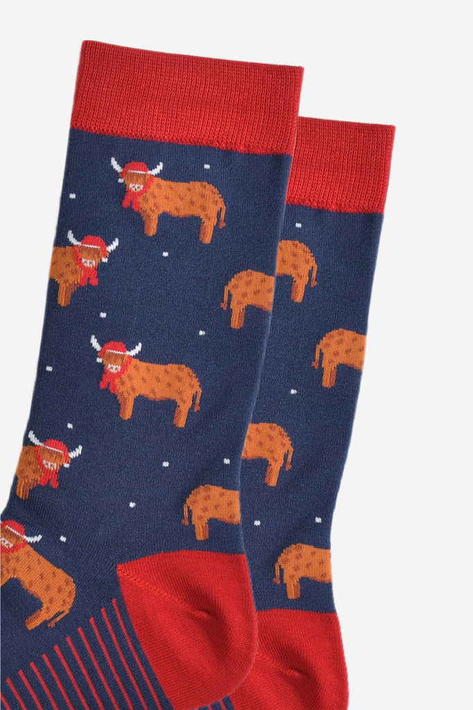 close up of the orange highland cows on the socks, the cows are standing up and they are designed to look like they have long hair, they are also wearing a red santa hat and scarf