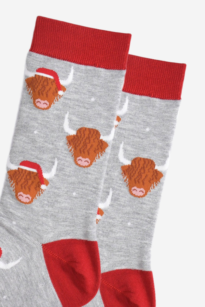 close up of the socks, showing the highland cow pattern where some of the cows are wearing santa hats, there is also a subtle white snowflake pattern on the socks