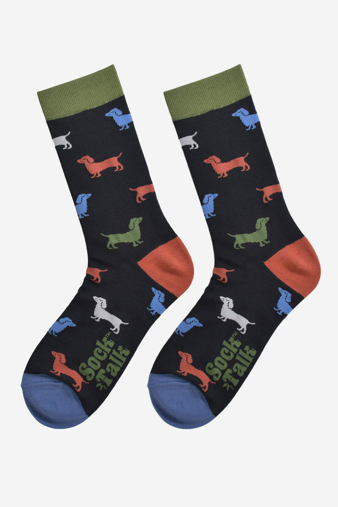 colourful sausage dog socks laying flat, showing the all over pattern of green, orange, blue and grey sausage dogs on a black sock