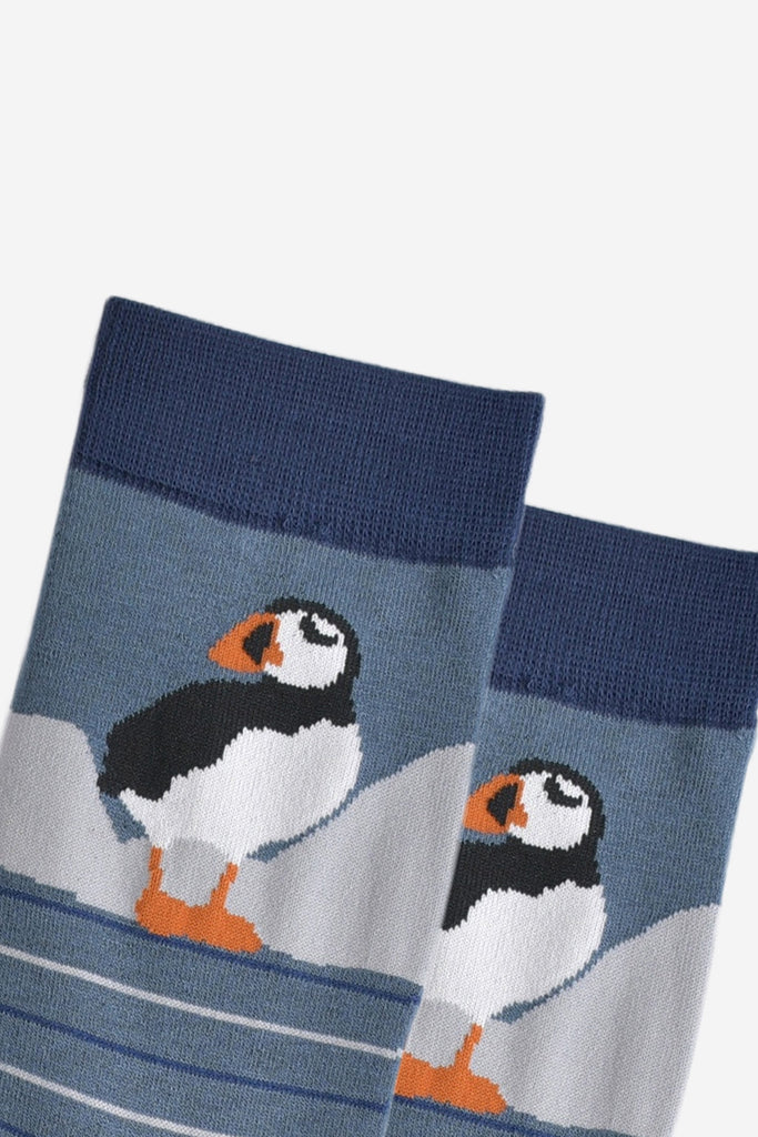 close up of the puffin, it is standing and has white cliffs behind it. 