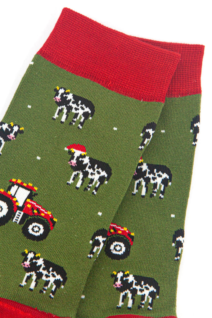 close up of the cow and tractor design on the socks, the cows are black and white, some are wearing santa hats. the tractors are red and have gold party lights on them. 