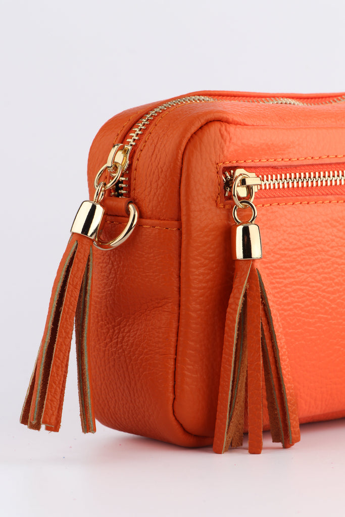 close up of the gold zip closure and tassel trim on the orange leather camera bag