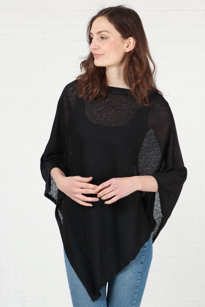 model wearing the plain black poncho styled with blue jeans. the material of the poncho is lightweight and transparent
