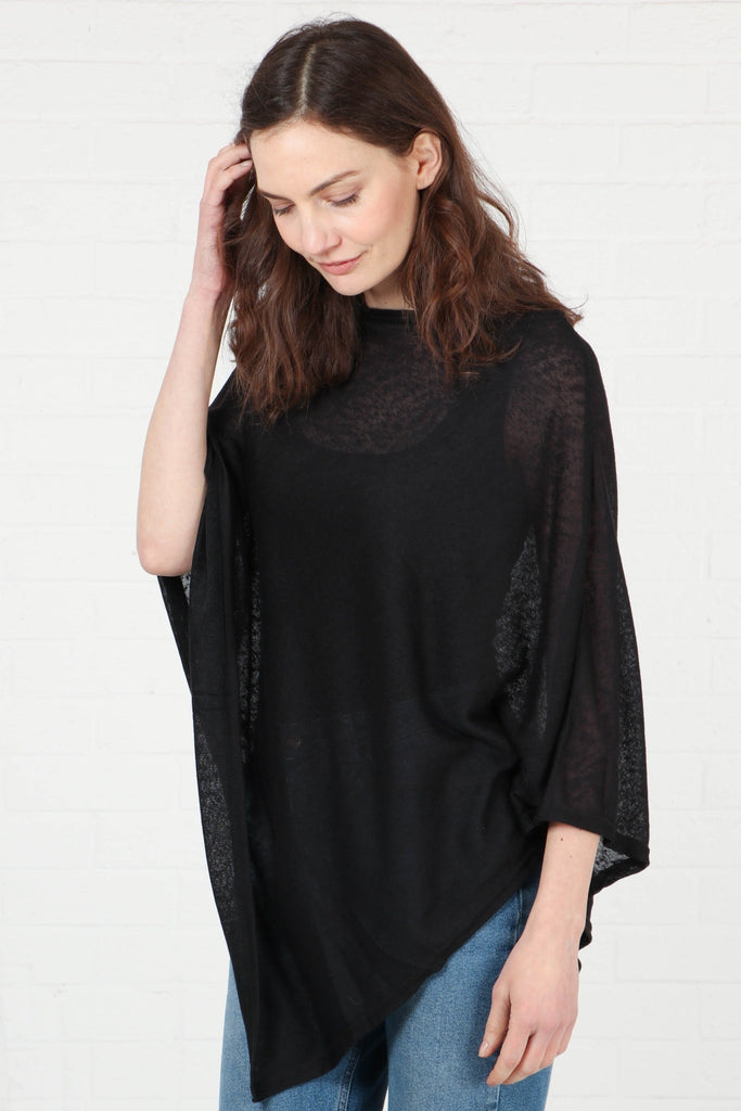 model wearing a plain black lightweight poncho with an asymmetrical hemline and short wide sleeves