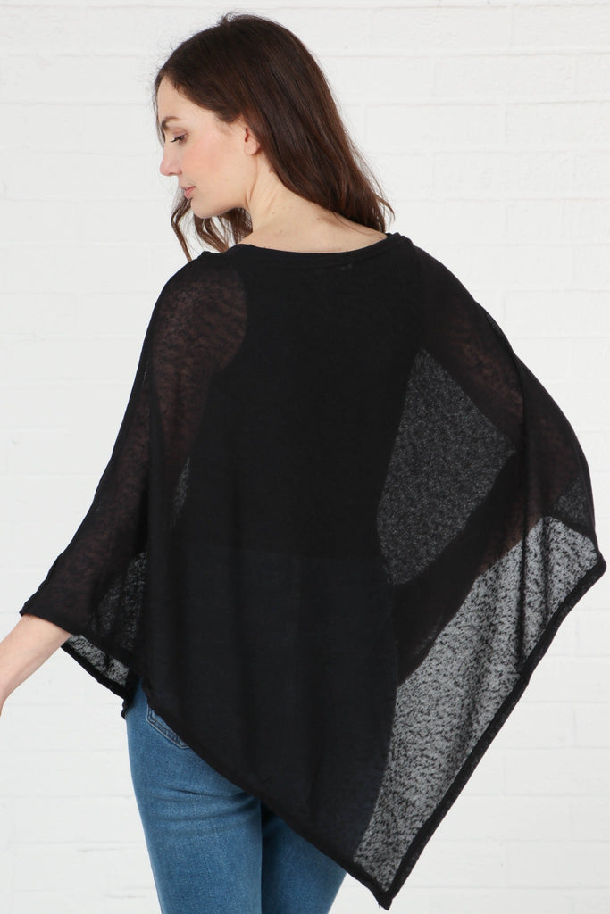 model showing the back of the plain black poncho, showing the asymmetrical design