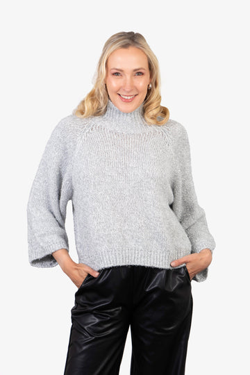 model wearing a silver sparkly knitted jumper, with a knitted high neck and an all over sparkly silver tinsel effect.