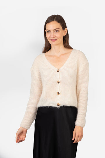 model wearing a cropped length beige knitted cardigan with a button up front