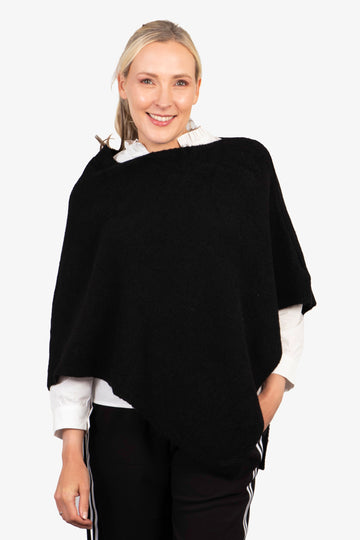 model wearing a black knitted asymmetrical poncho with a cowl neck