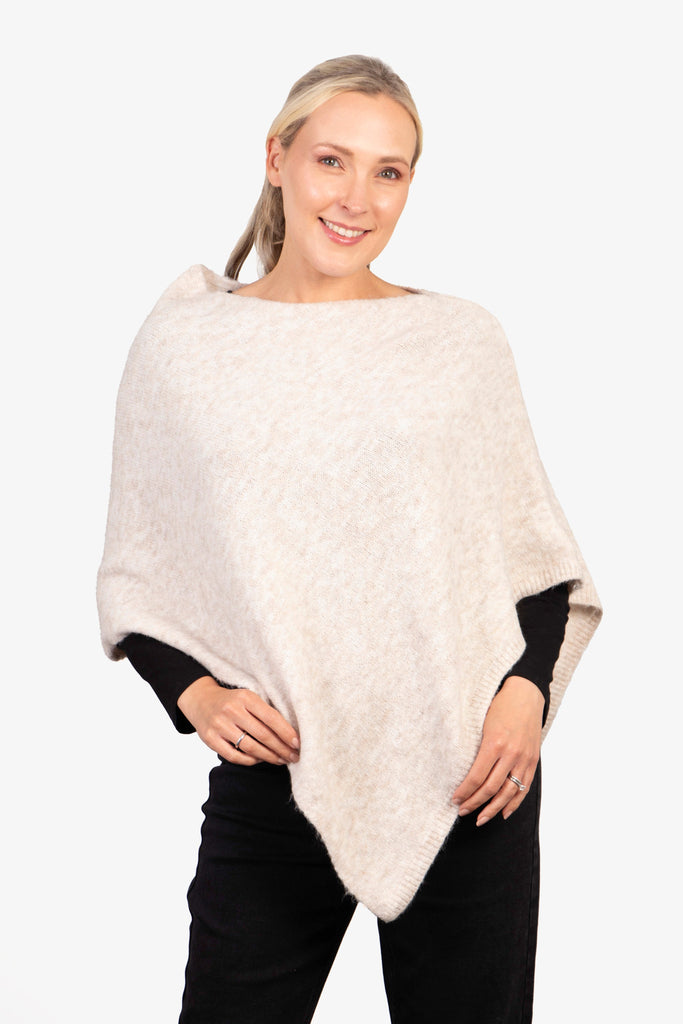 model wearing a cream knitted asymmetrical poncho with a cowl neck