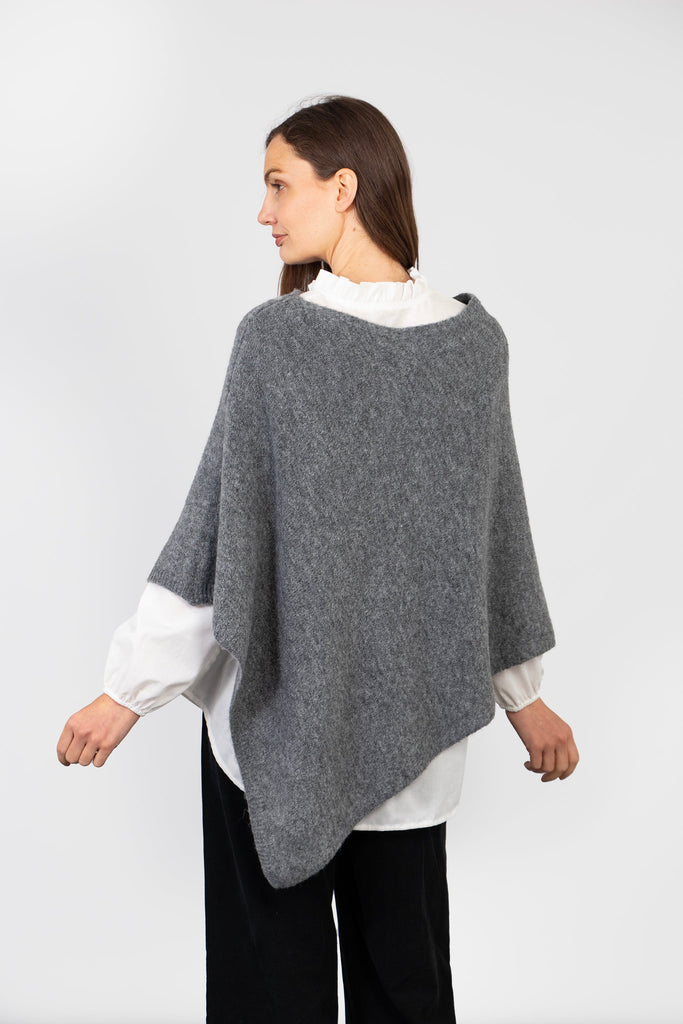 model showing the back of the grey poncho, highlighting the asymmetrical hem and plain pattern