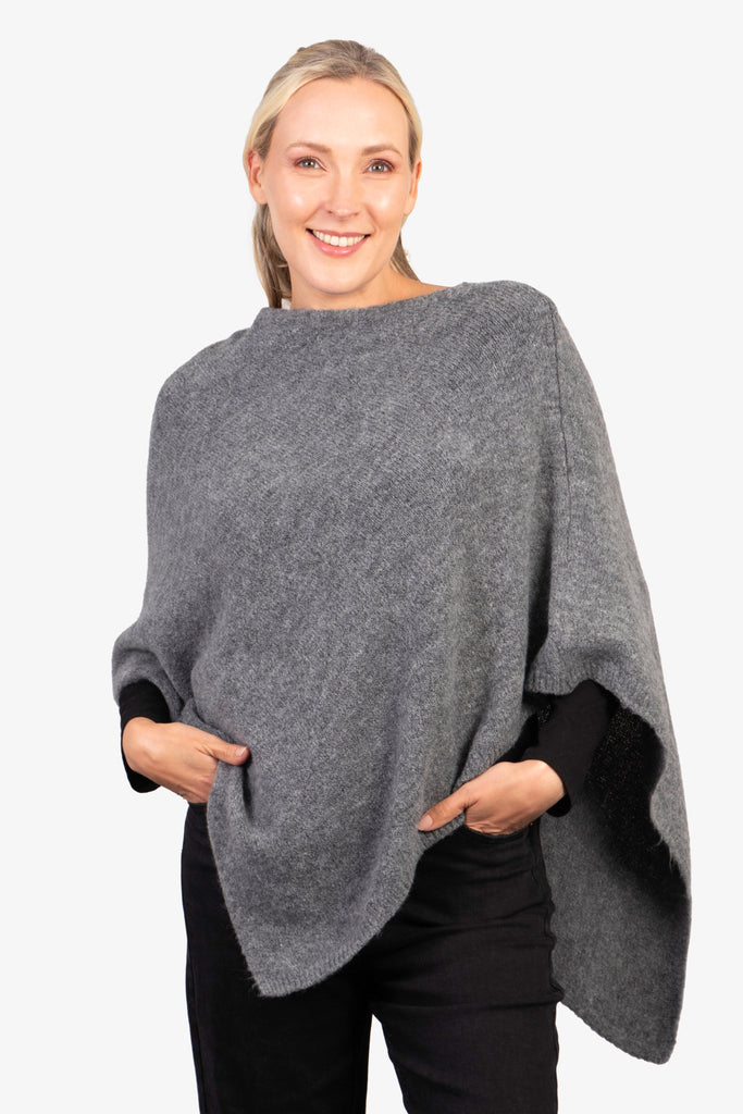 model wearing a grey knitted asymmetrical poncho with a cowl neck